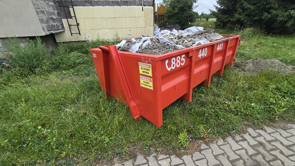 Czerwony kontener na gruz i odpady budowlane obok budynku, usługa Wywóz odpadów budowlanych