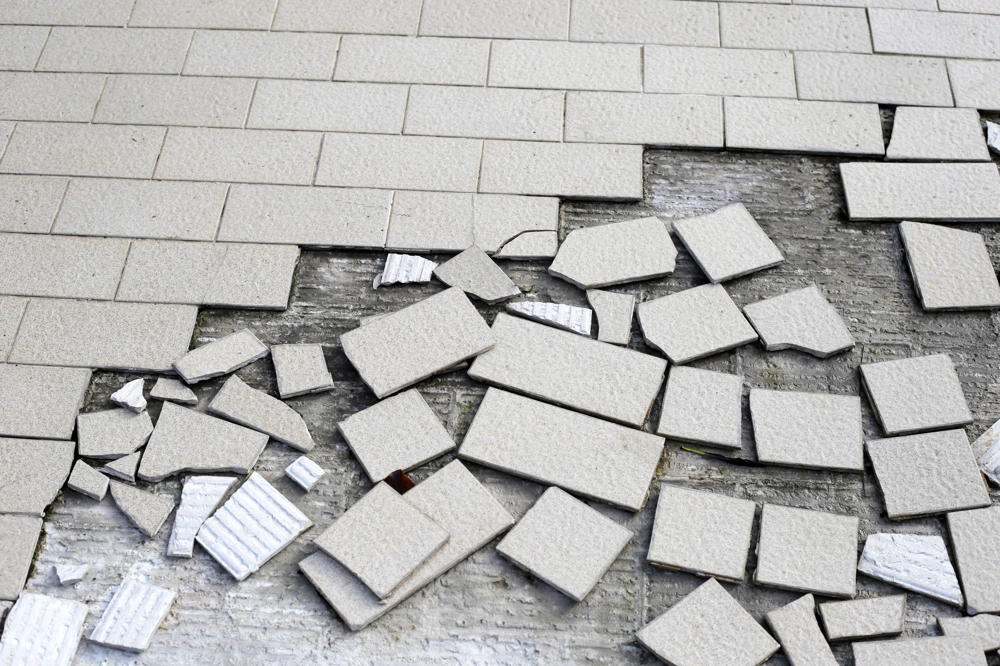 Rozbite kawałki jasnych płytek ceramicznych na betonowym podłożu, przygotowane do wywozu odpadów budowlanych